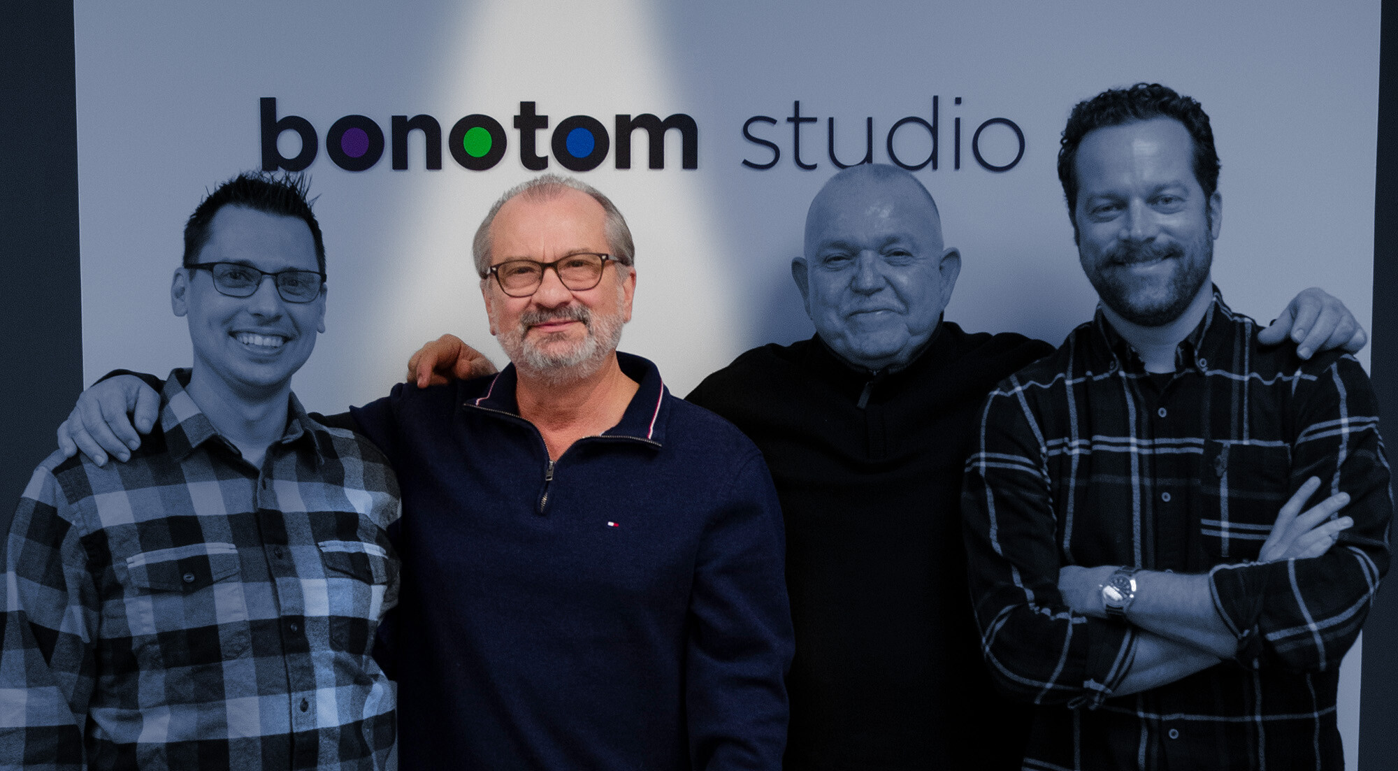 Group photo of bonotom employees in front of the BonoTom Studio logo with Tom spotlighted