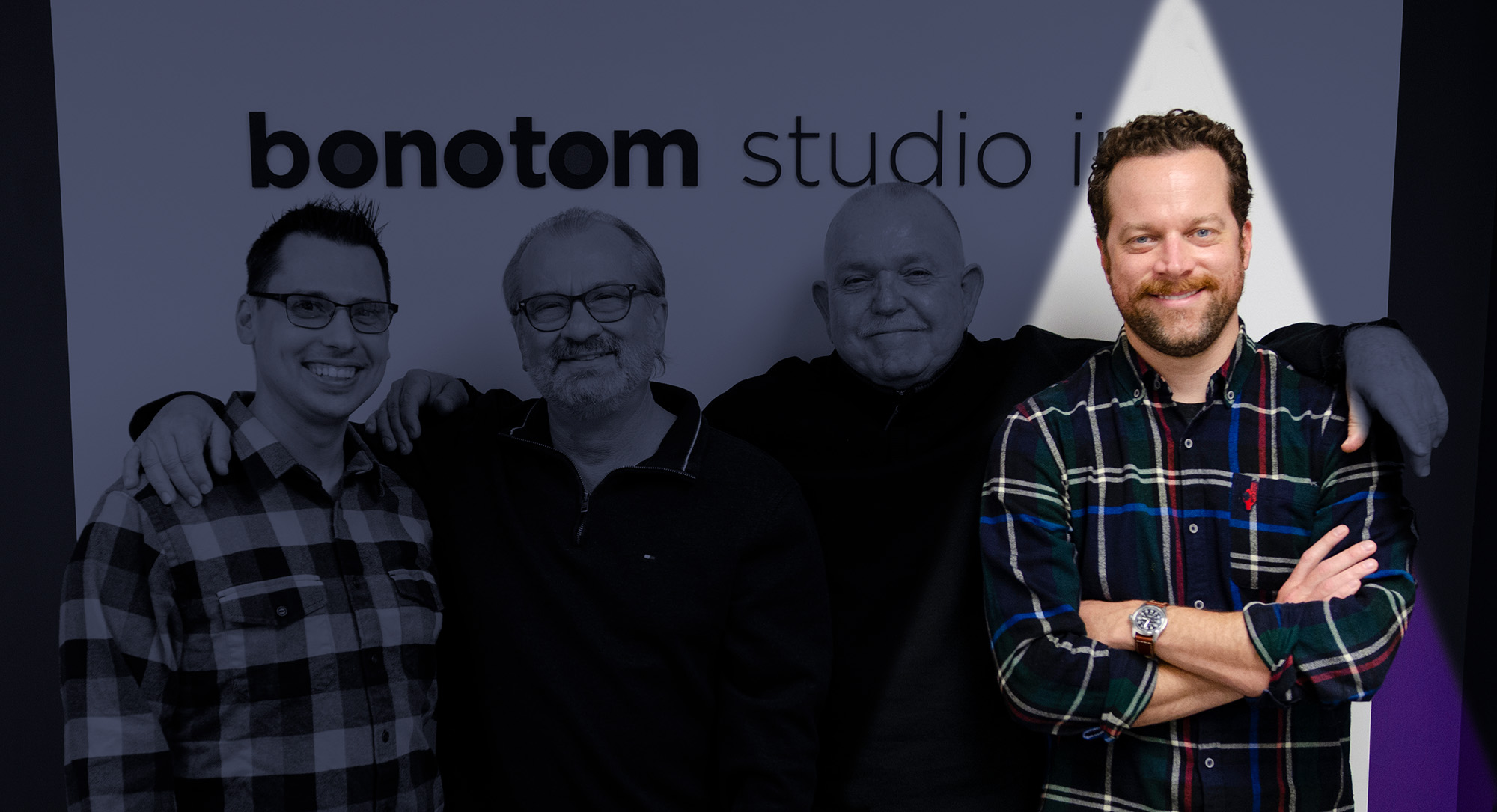 Four men smiling and posing in front of a wall with the logo "bonotom studio," with Paul Philpott and another man in the center embracing, while the others stand on the sides.